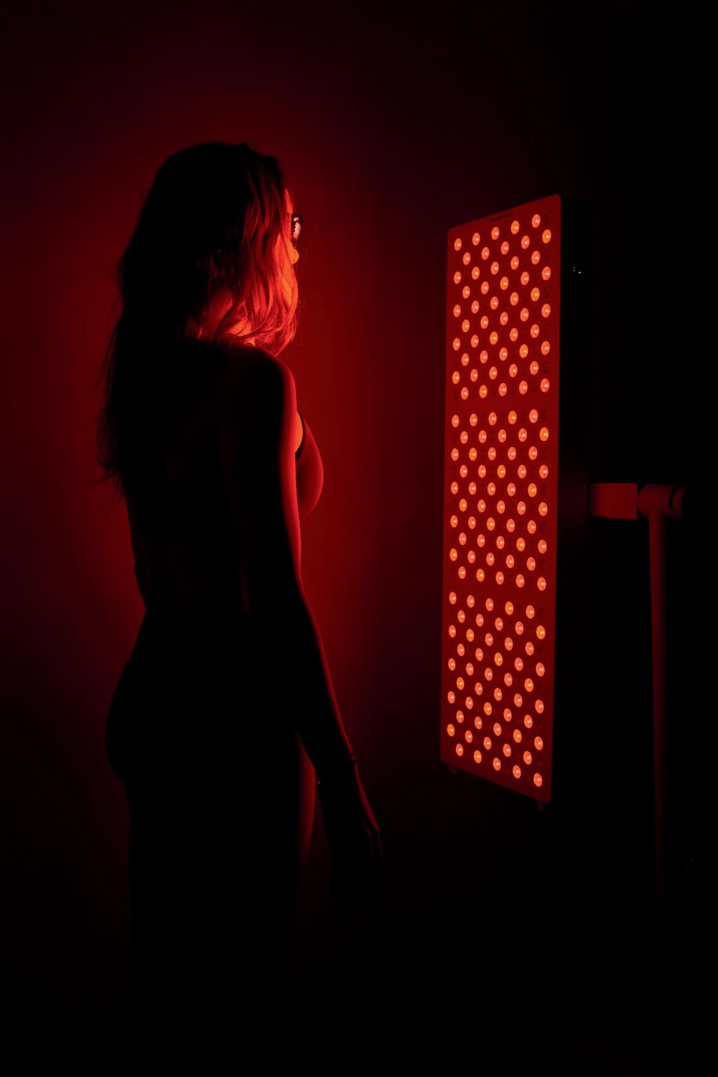 Persona de pie frente a un panel vertical de luces LED rojas.