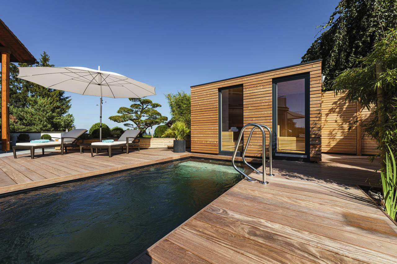 Sauna exterior de madera junto a una piscina y una terraza ajardinada
