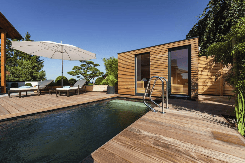 Sauna exterior de madera junto a una piscina y una terraza ajardinada